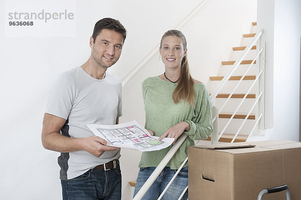 Couple discussing a blueprint by staircase in new home