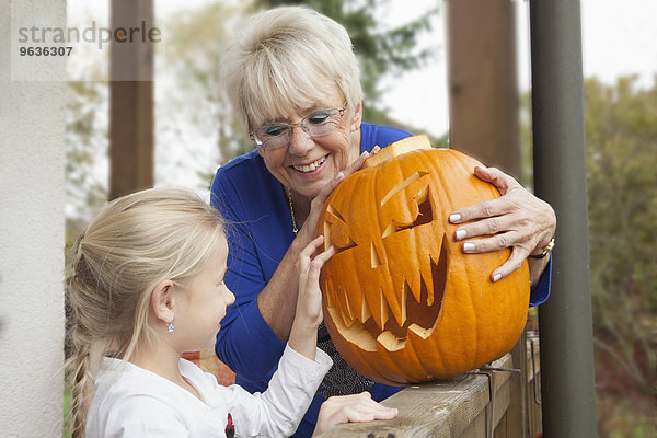 Senior woman showing Halloween pumpkin to her granddaughter