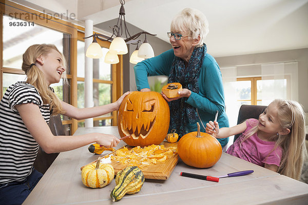 Senior woman carving pumpkin for Halloween with her granddaughters