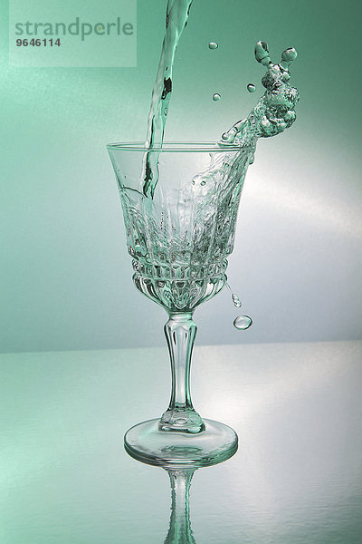 Wasser wird in ein Glas geschüttet und spritzt dabei zum Teil aus dem Glas heraus