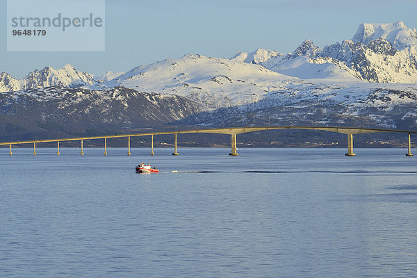 Rotes Boot vor der Hadselbrücke über den Sund  dahinter die verschneite Bergkulisse der Insel Hinnøya  Langøysund  bei Stokmarknes  Nordland  Vesterålen  Norwegen  Europa