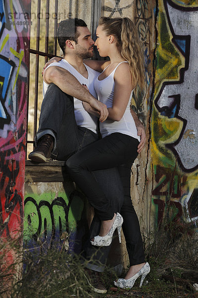 Küssendes junges Paar an einem vergitterten Fenster in einer mit Graffiti bemalten Ruine
