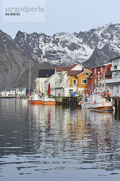 Fischerdorf mit Booten im Hafenbecken vor schneebedeckten Bergen der Insel Austvågøy  Henningsvær  Lofoten  Nordland  Norwegen  Europa