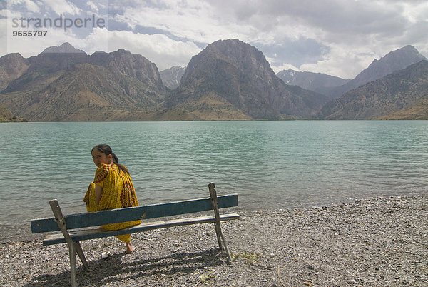 Frau auf Bank am türkisfarbenen Alexandersee in den Fanbergen  Iskanderkul  Tadschikistan  Zentralasien  Asien