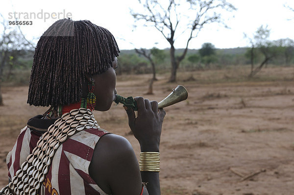 'Junge Frau vom Hamar Stamm bläst in ein Horn um Aufmerksamkeit zu erregen  beim Initiationsritual ''Sprung über die Rinder''  südliches Omotal  Äthiopien  Afrika'