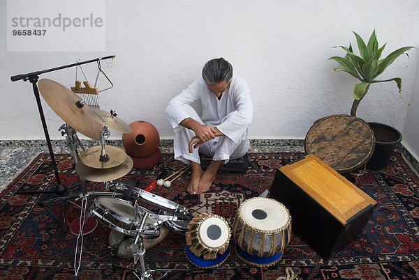 'Musiker  Anfang 40  sitzt inmitten seiner Perkussionsinstrumente  vor ihm Tablas  ein Schlaginstrument der nordindischen Musik  neben ihm eine Kistentrommel namens ''Cajon'''