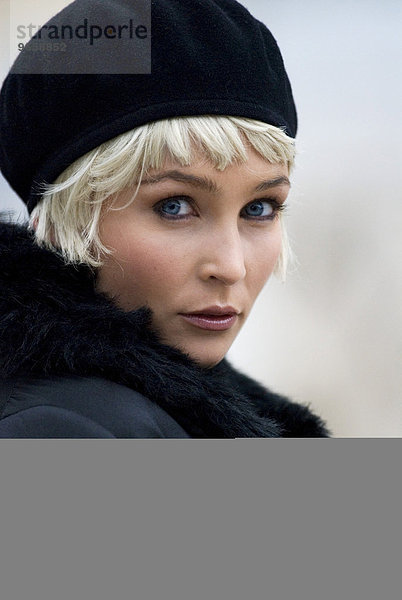 Portrait blonde Frau Anfang zwanzig in schwarzer Jacke und mit schwarzer Mütze