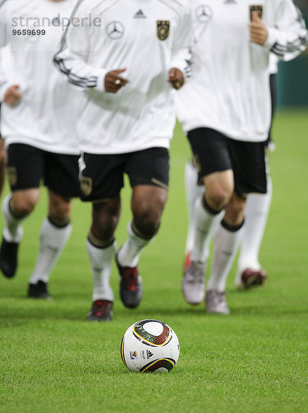 Jabulani  der offizielle Matchball der FIFA Weltmeisterschaft 2010 in Südafrika liegt auf dem Rasen  dahinter laufen sich deutsche Nationalspieler warm