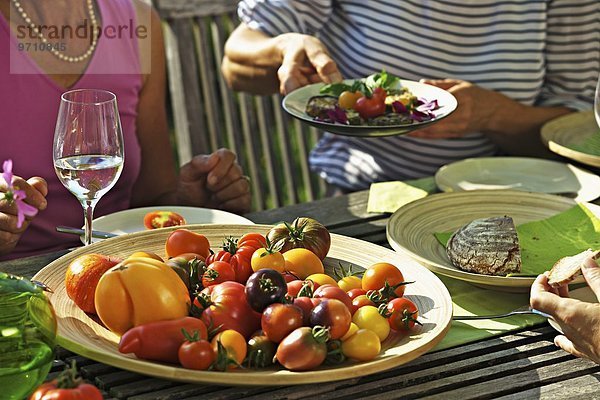 Menschen essen Tomaten auf einem sommerlichen Gartentisch