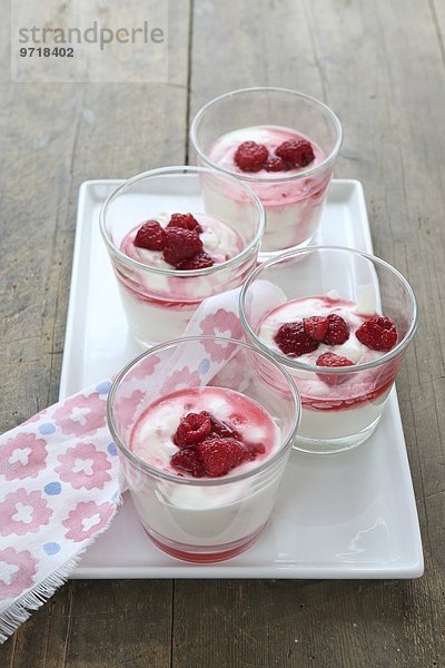 Vanillejoghurt mit Himbeeren in Dessertgläsern auf Porzellanteller