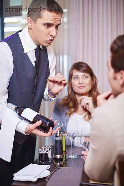 Kellner zeigt Geschäftspartnern Weinflasche im Hotelrestaurant