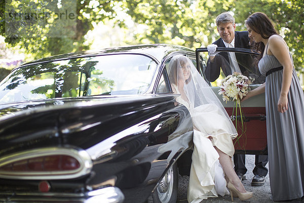 Braut  die vor ihrer Hochzeit mit Fahrer und Trauzeugin aus dem Auto steigt