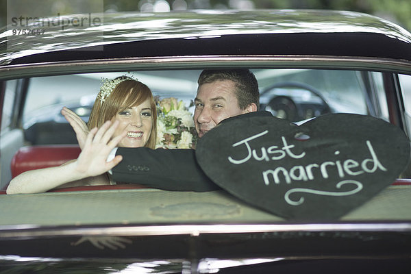 Glückliche Braut und Bräutigam winken im Auto nach der Hochzeit