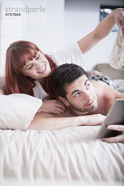 Junges Paar im Bett liegend Frau zeigt Mann ihre Dessous