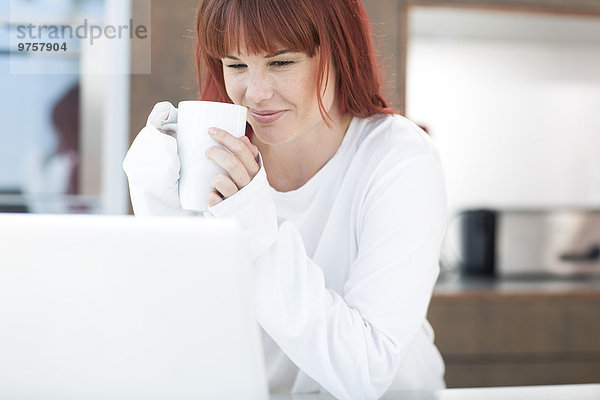 Junge Frau mit Laptop und Tasse Kaffee in der Küche