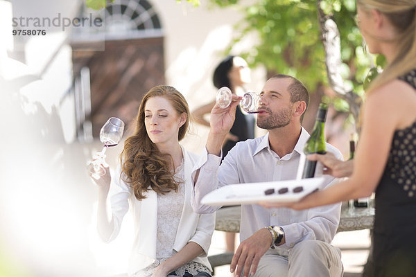 Kellnerin mit Tablett und Paar im Freien sitzend  Rotweinverkostung
