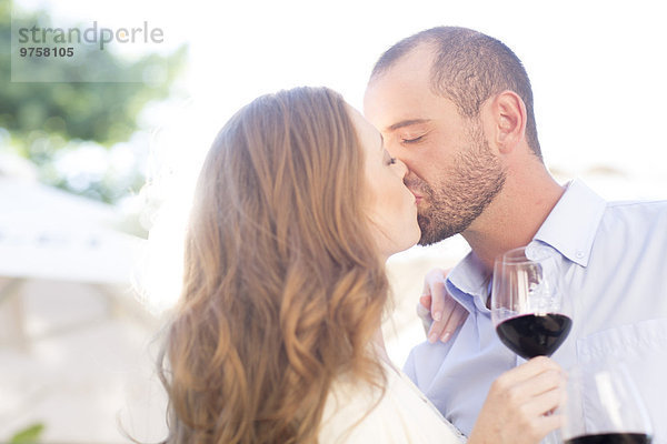 Paar mit Weingläsern und Küssen im Freien