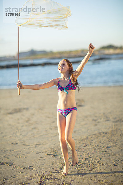 Fröhliches Mädchen am Strand  das mit einem Schmetterlingsnetz läuft.