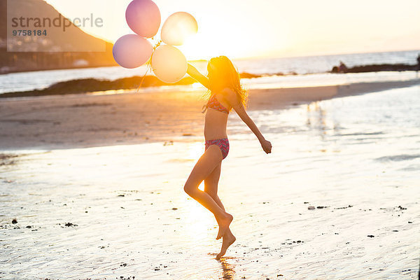 Mädchen am Strand mit Luftballons bei Sonnenuntergang