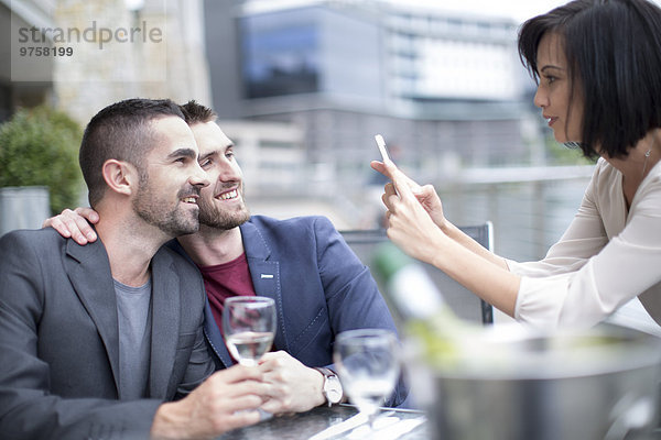 Schwules Paar beim Essen und Freund beim Fotografieren mit dem Handy