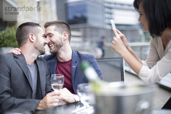 Schwules Paar beim Essen und Freund beim Fotografieren mit dem Handy