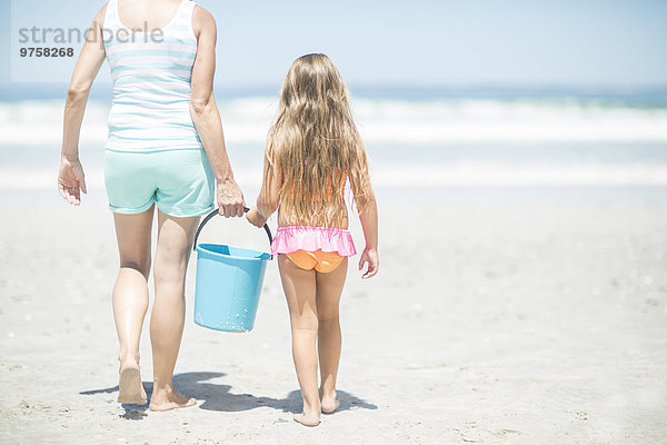 Mutter und Tochter am Strand spazieren gehen mit einem Eimer