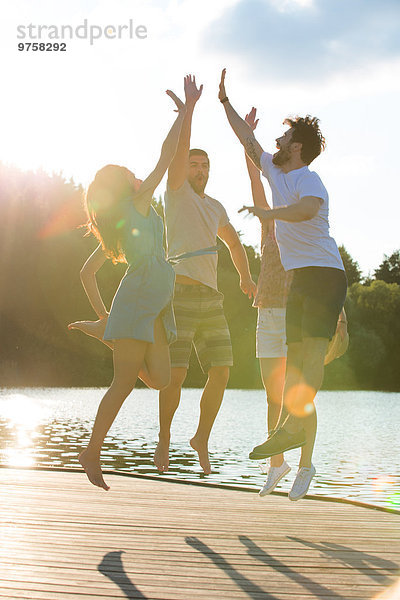 Vier Freunde beim Fiving an einem See im Gegenlicht