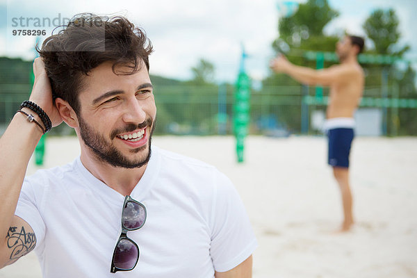 Lächelnder junger Mann auf dem Beachvolleyballfeld
