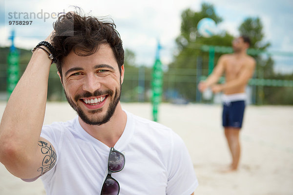 Lächelnder junger Mann auf dem Beachvolleyballfeld