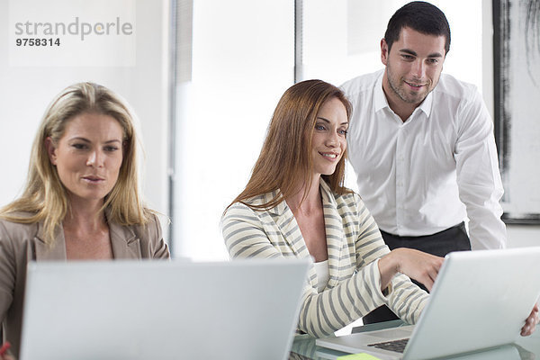 Geschäftsfrauen und Geschäftsleute im Büro bei der Arbeit an Laptops