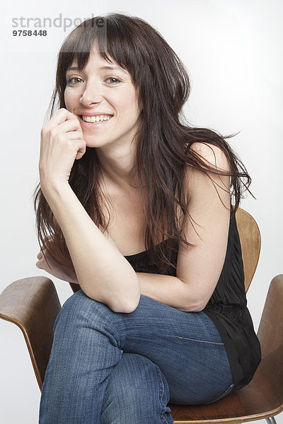 Porträt einer lächelnden Frau mit dunklen langen Haaren auf einem Stuhl sitzend