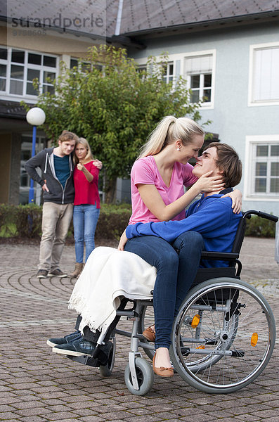 Junge Frau  die ihren Freund im Rollstuhl umarmt
