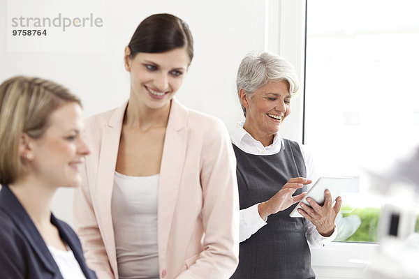 Drei lächelnde Geschäftsfrauen mit digitalem Tablett im Büro