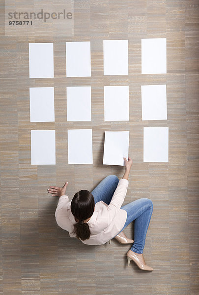 Geschäftsfrau sitzt auf dem Boden und organisiert leere Papierbögen.