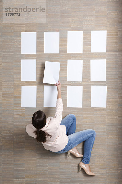 Geschäftsfrau sitzt auf dem Boden und organisiert leere Papierbögen.