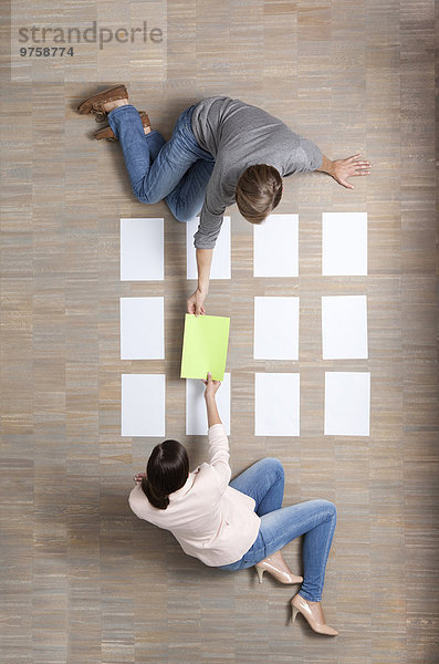 Geschäftsmann und Geschäftsfrau sitzen auf dem Boden und organisieren leere Papierbögen.