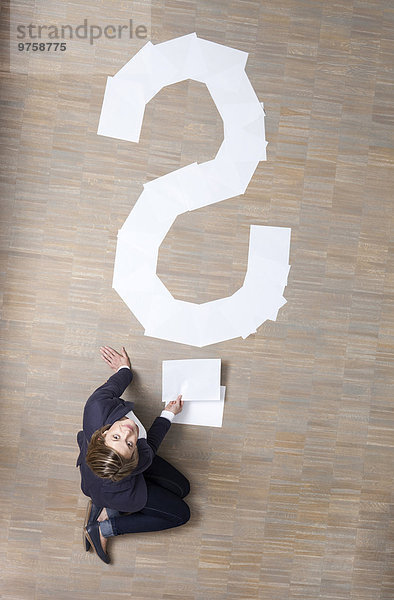 Geschäftsfrau auf dem Boden sitzend mit leeren Blatt Papier in Form eines Fragezeichens