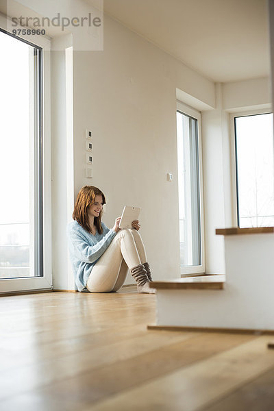 Junge Frau auf dem Boden sitzend mit digitalem Tablett