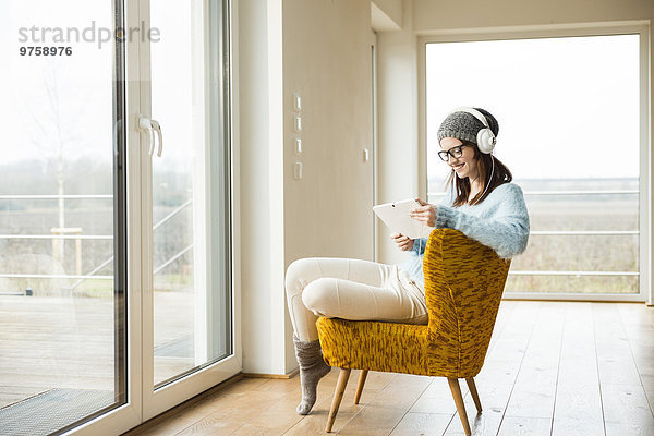 Lächelnde junge Frau sitzend auf Stuhl mit digitalem Tablett und Kopfhörer