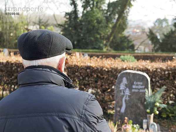 Alter Mann auf dem Friedhof beim Betrachten des Grabsteins