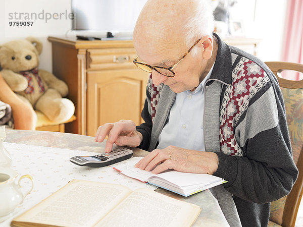 Alter Mann am Tisch auf der Suche nach Telefonnummer im Notizbuch