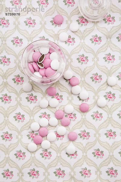 Glas mit rosa und weißen Schokoladenknöpfen auf floral gemustertem Stoff