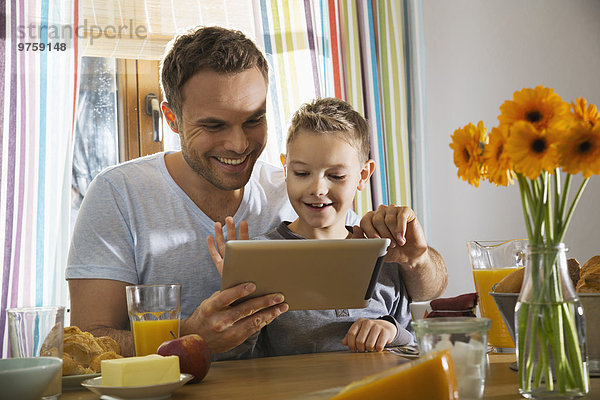 Vater und Sohn sitzen am Frühstückstisch mit Hilfe eines digitalen Tabletts.