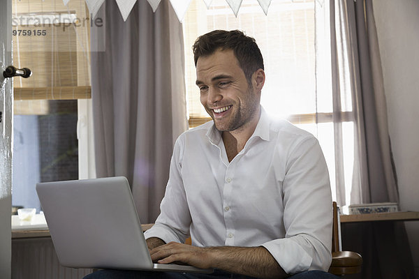 Lachender Mann bei der Arbeit mit dem Laptop in seinem Home-Office