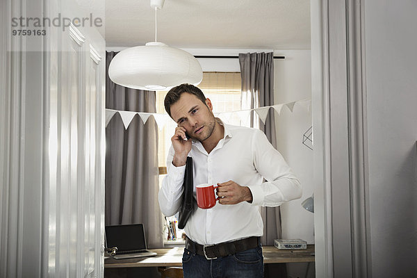 Geschäftsmann mit Kaffeetassen-Telefonie im Home-Office
