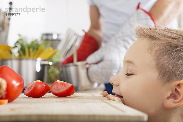 Lächelnder Junge schaut auf Tomatenscheiben auf dem Küchenbrett