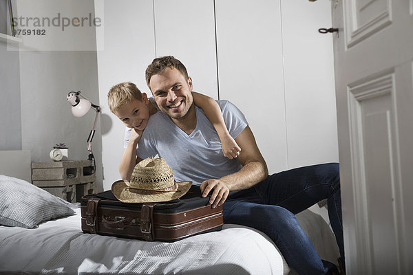 Vater und Sohn auf dem Bett sitzend mit Koffer und Strohhut