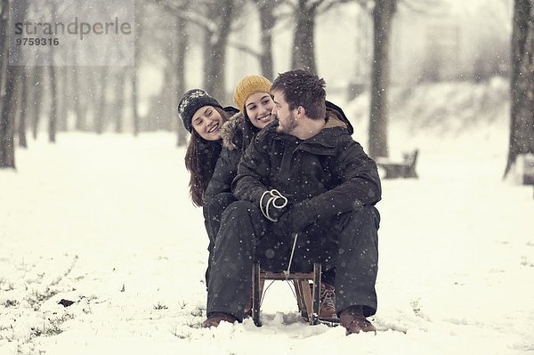 Drei Freunde sitzen im Winter auf dem Schlitten
