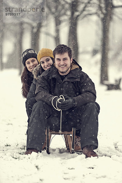 Gruppenfoto von drei Freunden  die im Winter auf dem Schlitten sitzen.