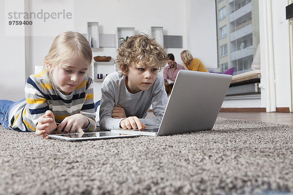 Geschwister auf dem Boden liegend mit Laptop und digitalem Tablett